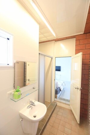 Un baño con lavamanos blanco, un espejo y repisa de vidrio.