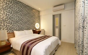 A hotel room with a bed, a bedside table with a lamp, a wall-mounted mirror, and a door with a curtain. - Yapo Bed and Breakfast (Luodong)