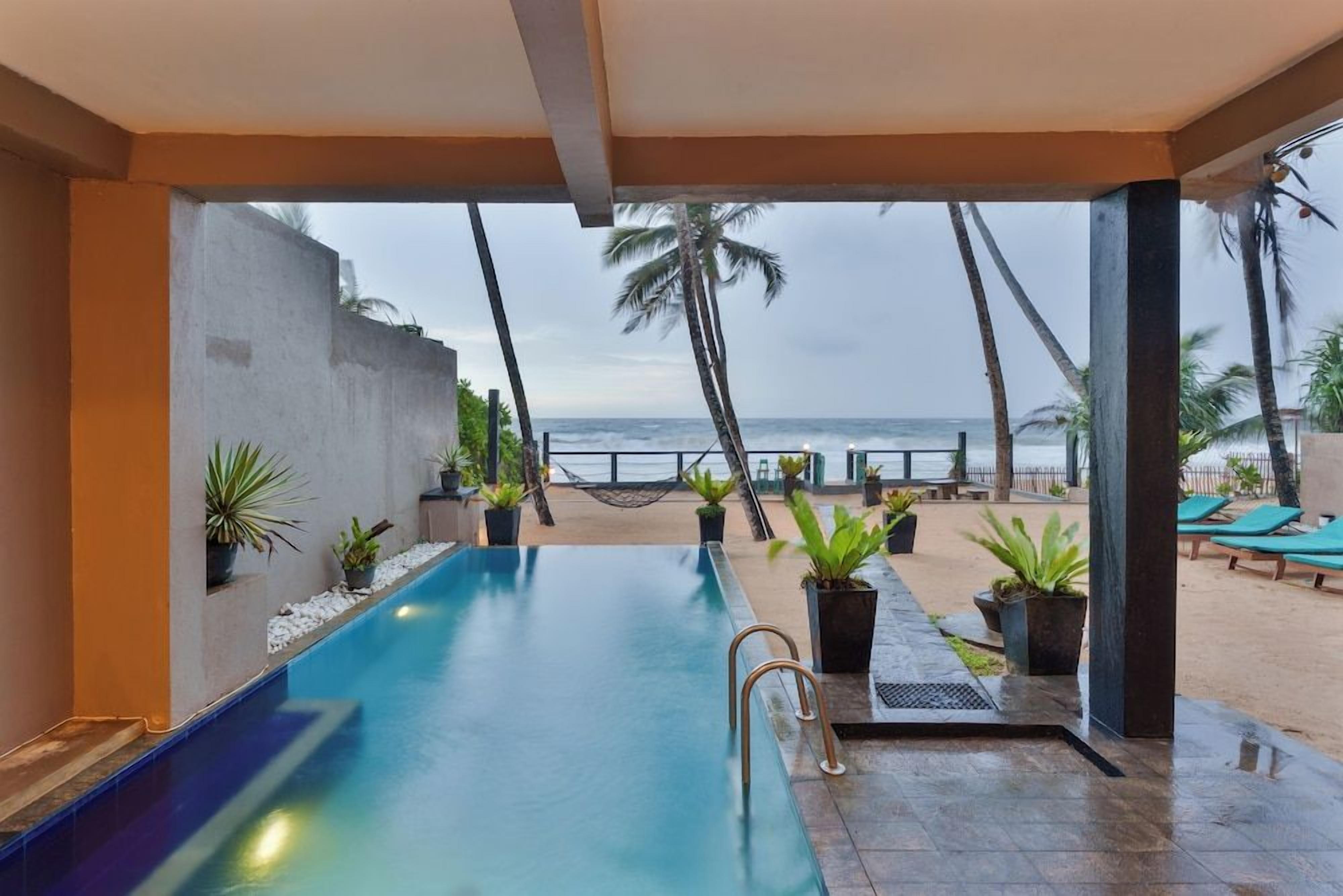 A swimming pool with a view of the beach and palm trees.