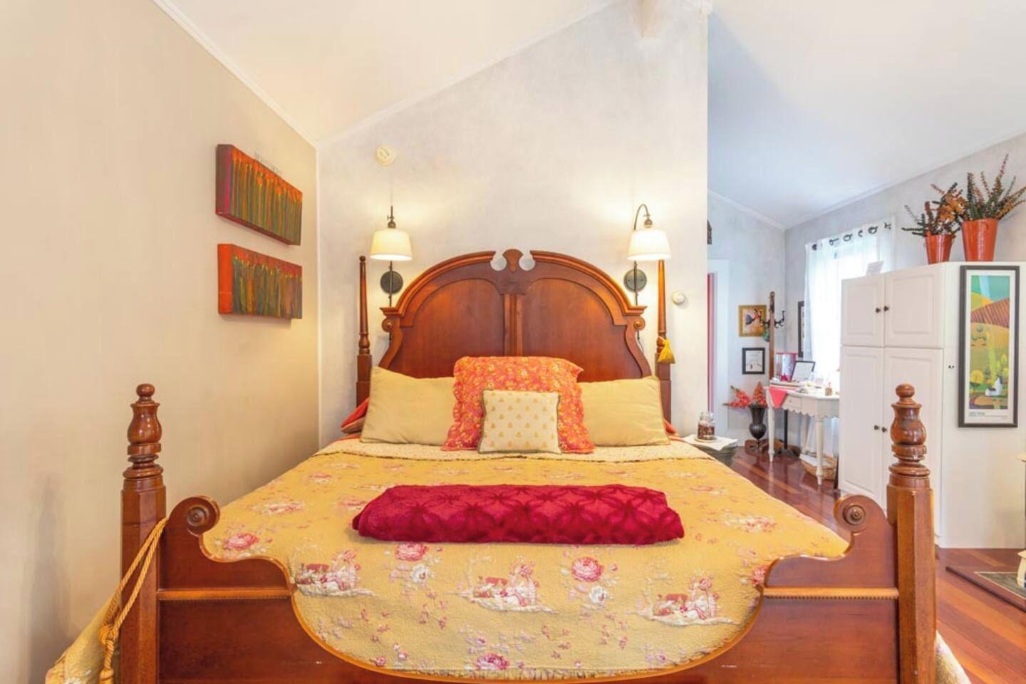 Een slaapkamer met een houten bed, een bloemenprint beddeken en twee wandlampen.