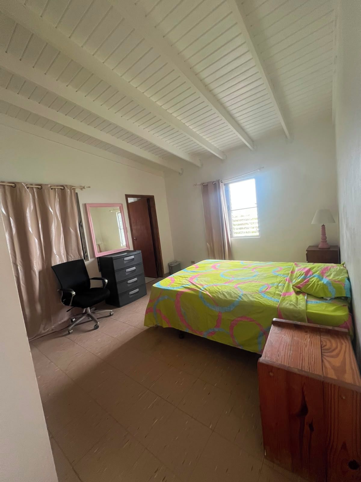 A bedroom with a bed, a desk, a chair, a dresser, and a window with curtains.
