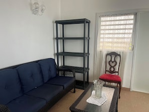 Un salon avec un canapé bleu foncé, une table basse en verre, une étagère en métal noir et une chaise en bois avec un coussin rouge.