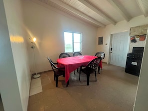 Un coin repas avec une table dressée pour quatre personnes, une fenêtre et un espace cuisine équipé d’une cuisinière.