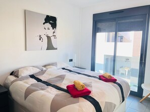 A hotel room with a large bed, a painting on the wall, and a view of the outside through a glass door. - Sunny Apartment in La Zenia for 4 (Orihuela)