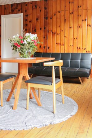 Una mesa de comedor de madera con sillas, un sofá negro y un centro de mesa floral.