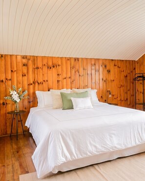 A bedroom with a wooden paneled wall, a bed with white bedding, and a small table with a vase of flowers. - Casa Pnoē (Campos do Jordão)
