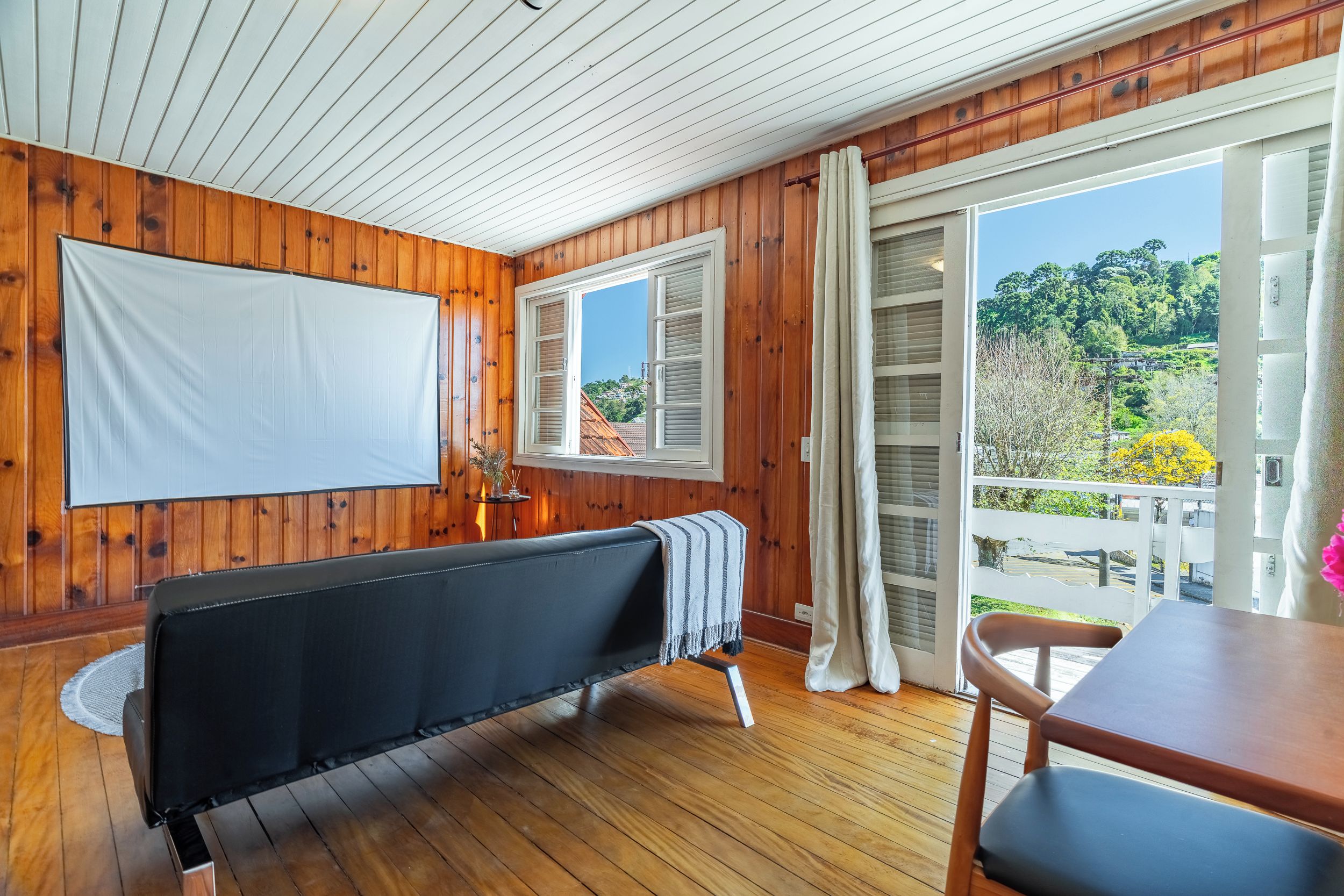A room with wooden walls, a black sofa, a table, and a window with shutters.