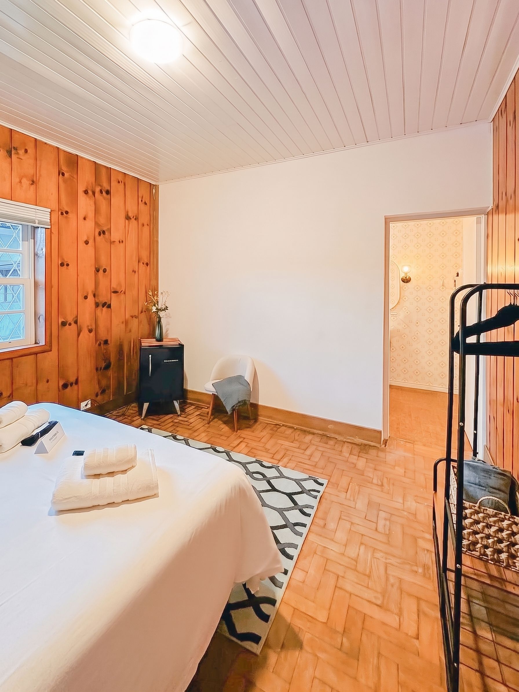 A hotel room with a bed, a small table, a chair, a desk, and a wardrobe.