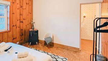 A hotel room with a bed, a small table, a chair, a desk, and a wardrobe.