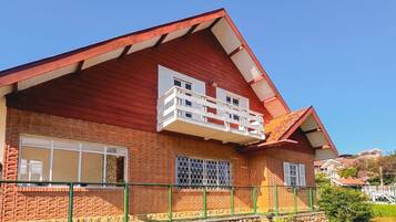 A two-story house with a red roof, a balcony on the second floor, and a stone foundation.