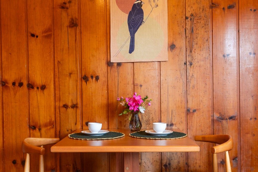 A wooden table with two white cups and a vase of pink flowers against a wooden wall.