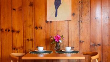 A wooden table with two white cups and a vase of pink flowers against a wooden wall.