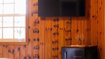 A room with wooden walls, a bed with white bedding, a black entertainment unit with a flat-screen TV, and a window with a view.