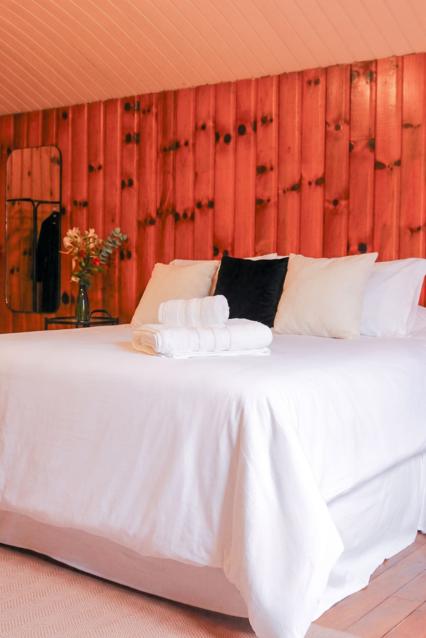 A hotel room with a wooden paneled wall, a bed with white linens, and a vase with flowers on the nightstand.