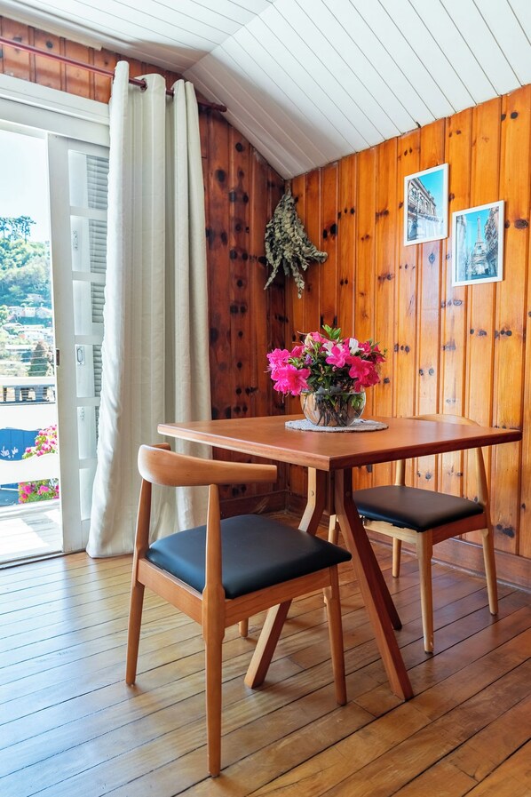 A wooden-paneled room with a table and chairs, a window with curtains, and a wall-mounted picture. - Casa Pnoē (Campos do Jordão)