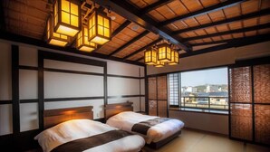 A traditional Japanese-style room with tatami flooring, two beds with dark headboards, and a view of buildings through large windows. - Kanazawa no Yado Yuyarurusaisai (Kanazawa)
