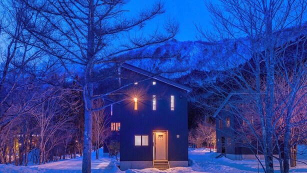 A modern two-story building with a dark exterior, a visible entrance, and a snow-covered ground. - Powdersuites (Hakuba)