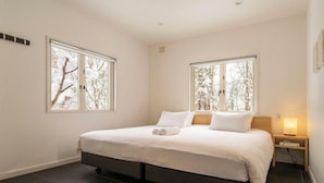 A bedroom with a bed, two windows, a nightstand, and a wall-mounted lamp. - Powdersuites (Hakuba)