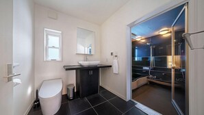 A modern bathroom with a white toilet, a sink with a mirror, and a shower area. - Powdersuites (Hakuba)