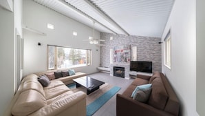 A modern living room with a stone accent wall, a fireplace, and a flat-screen TV. - Powdersuites (Hakuba)