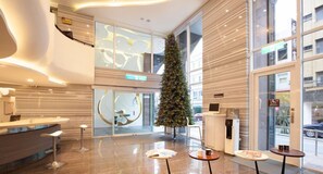 A modern hotel lobby with a reception desk, a Christmas tree, and a large window offering a view of the street. - Yanold Fashion Spring House (Jiaoxi)