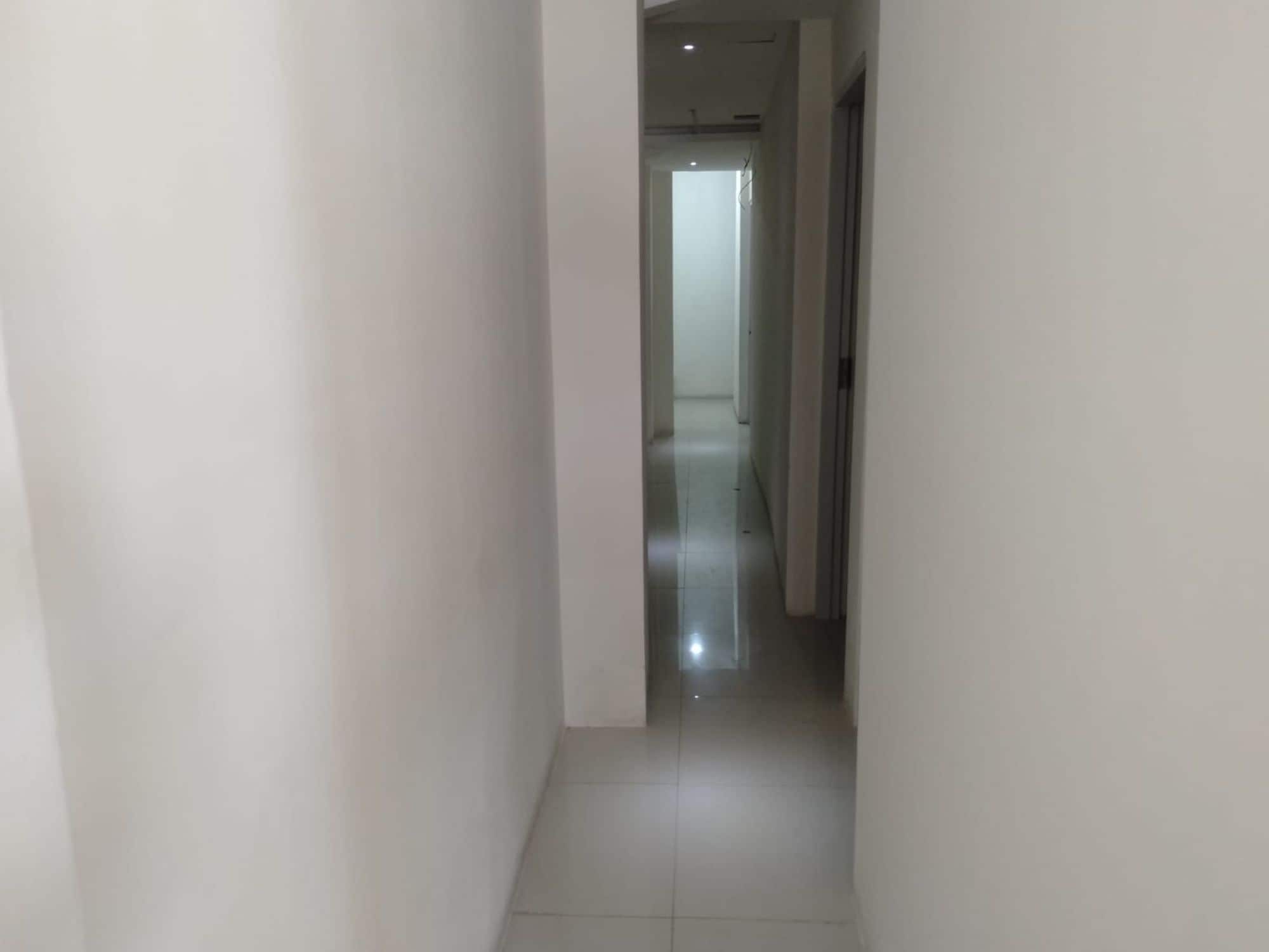 A narrow, tiled hallway with white walls and a door at the end.