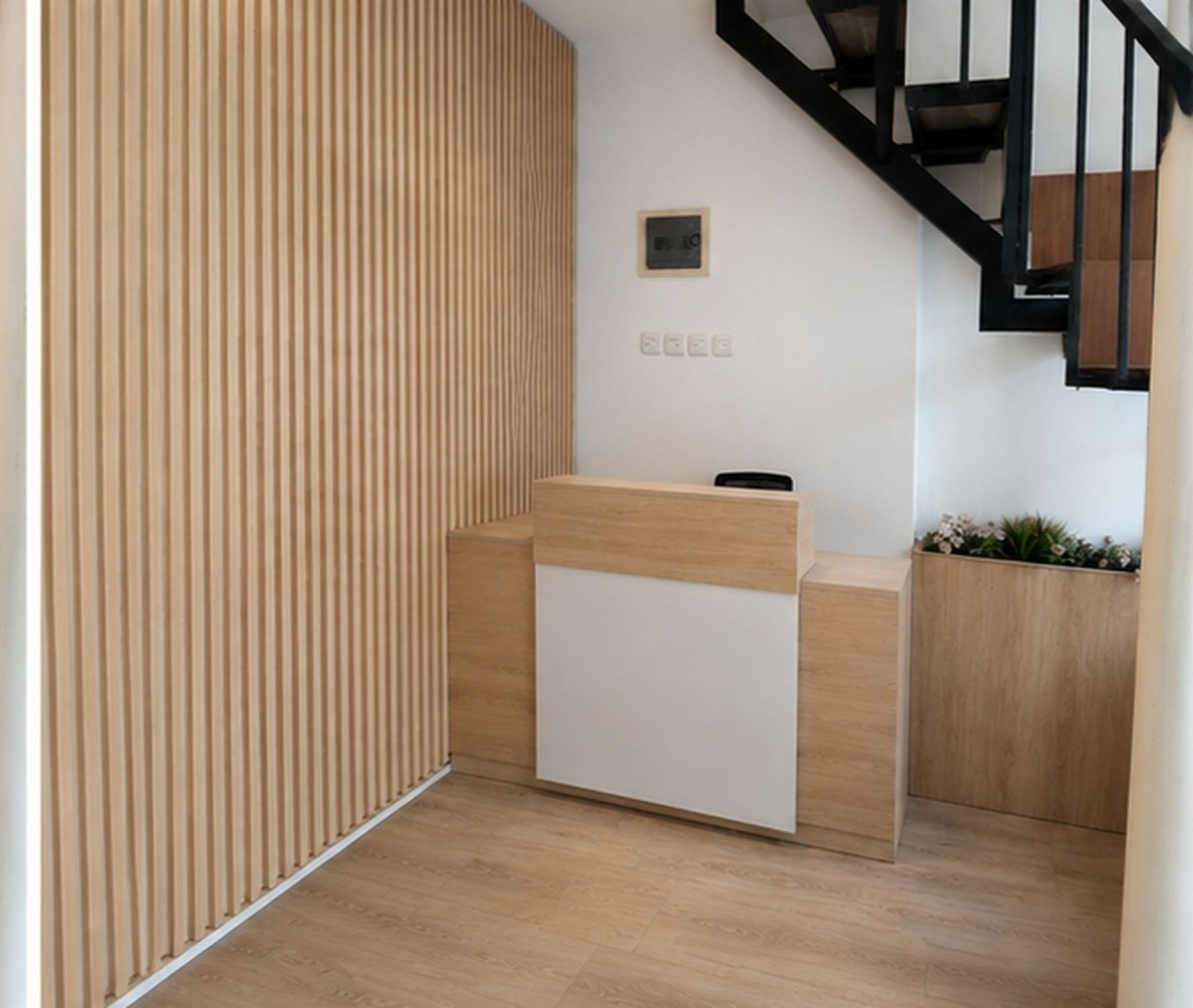 A reception desk with a wooden panel wall, a small plaque, and a staircase with black railings.