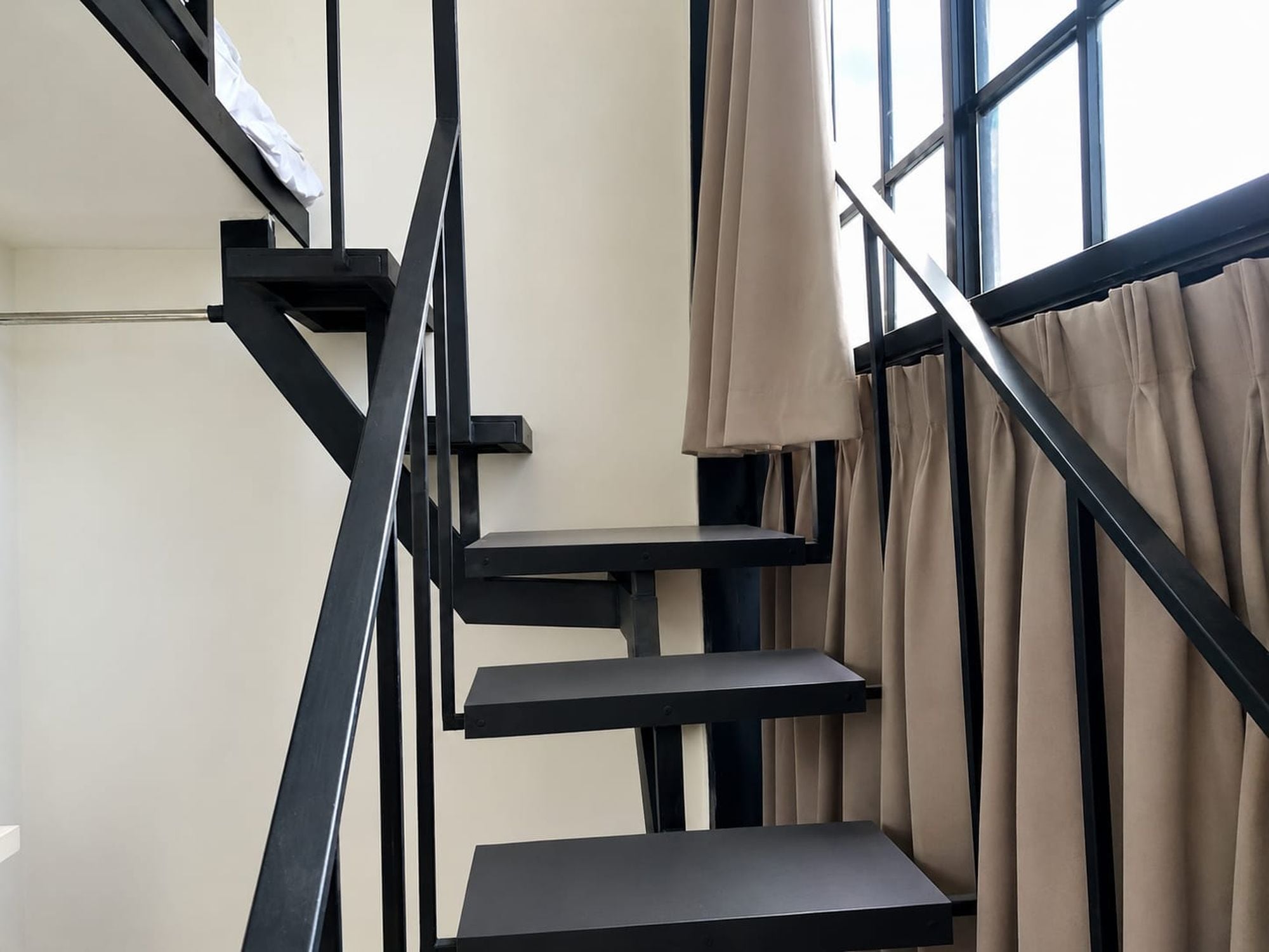 A staircase with black railings and beige curtains.