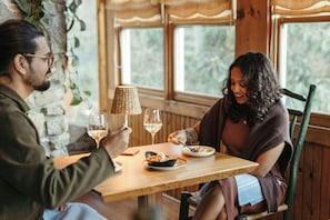 A wooden table with a woven lamp, two wine glasses, and a plate of food. - Highlands Inn Lodge Formerly Hampton Inn Highlands (Highlands)