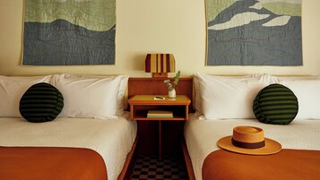 Habitación de hotel con dos camas, una mesita de noche con un libro y un control remoto, y una lámpara de pared.