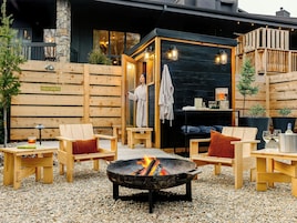 A wooden outdoor seating area with a fire pit, a wooden cabin labeled 'COLD SPRITZ,' and a person in a robe.