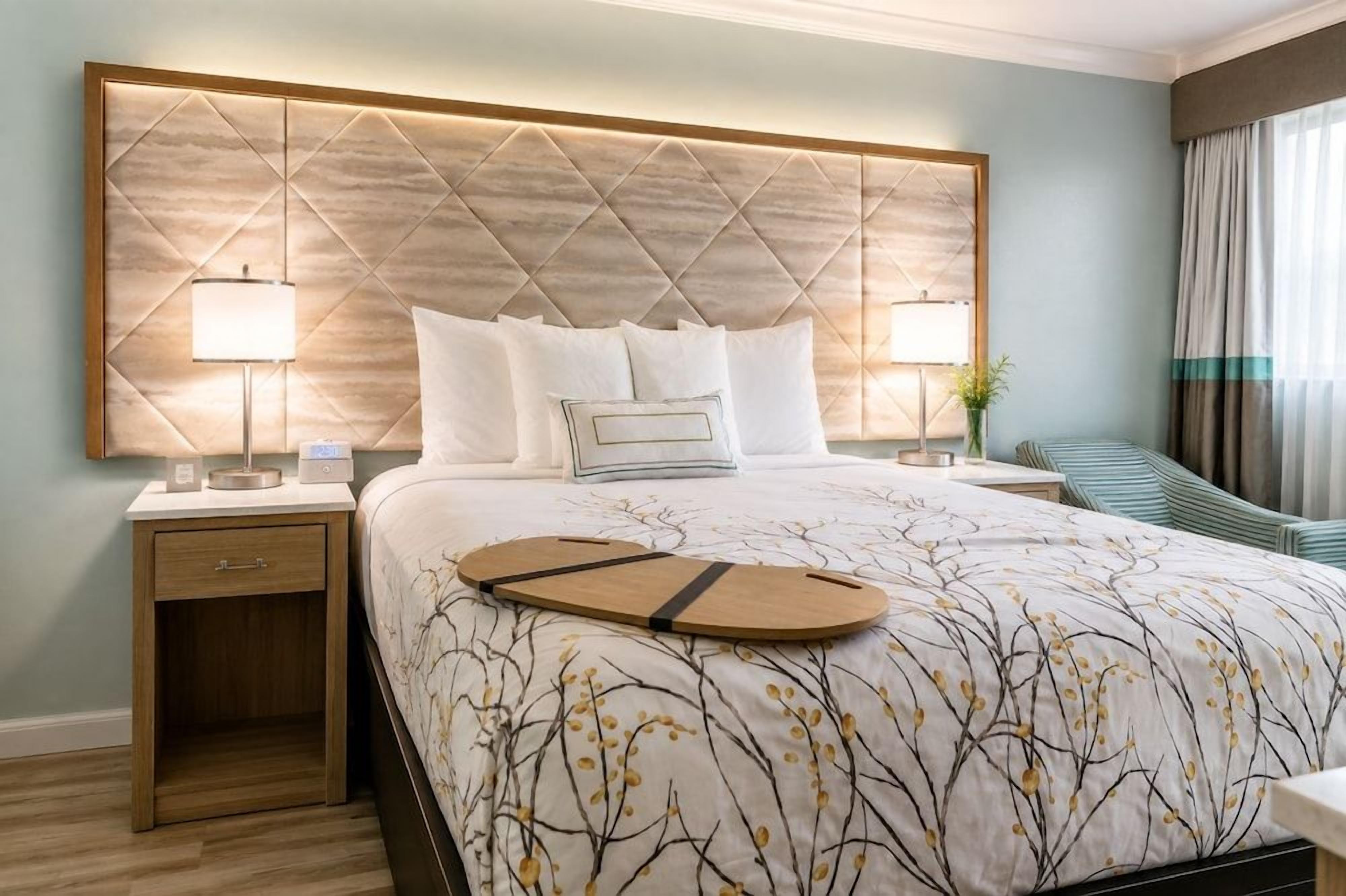 Habitación de hotel con una cama grande, dos mesitas de noche y vistas al exterior.