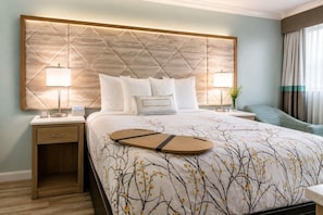 A hotel room with a large bed, two bedside tables, a nightstand, and a view of the outdoors. - Outer Banks Inn (Kill Devil Hills)