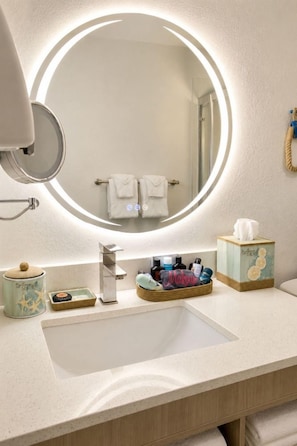 A bathroom with a round mirror, a sink, and a towel rack. - Outer Banks Inn (Kill Devil Hills)