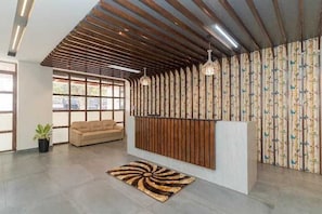 Una zona de recepció amb un sostre de llistons de fusta, un sofà, una cortina amb dibuixos i una catifa al sòl.