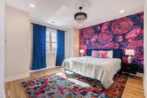 Een slaapkamer met een groot bed, een kleurrijk vloerkleed, een bloemen behang en een kroonluchter.