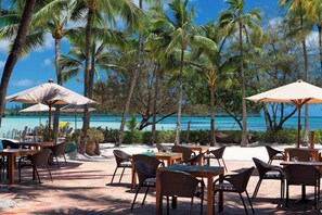Un espace de restauration en plein air, avec des tables et des chaises, entouré de palmiers et offrant une vue sur la plage.