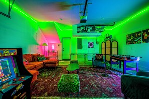 Ein Zimmer mit einem Retro-Spielautomaten, einer Couch, einem kleinen Tisch und einer Dartscheibe.