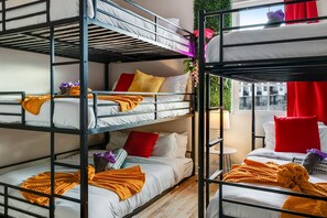 A bunk bed room with multiple beds, a small table, and a window with a view.