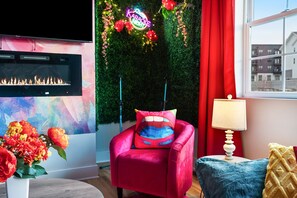 A room with a fireplace, a vibrant red chair, a wall-mounted TV, and a neon sign indicating a karaoke event. - The Vivid - Rooftop Hot Tub/Game Room/Sleeps 16 (Nashville)