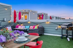 Eine Terrassengruppe im Freien mit Esstisch für vier Personen, umgeben von Korbmöbeln und roten Stühlen.