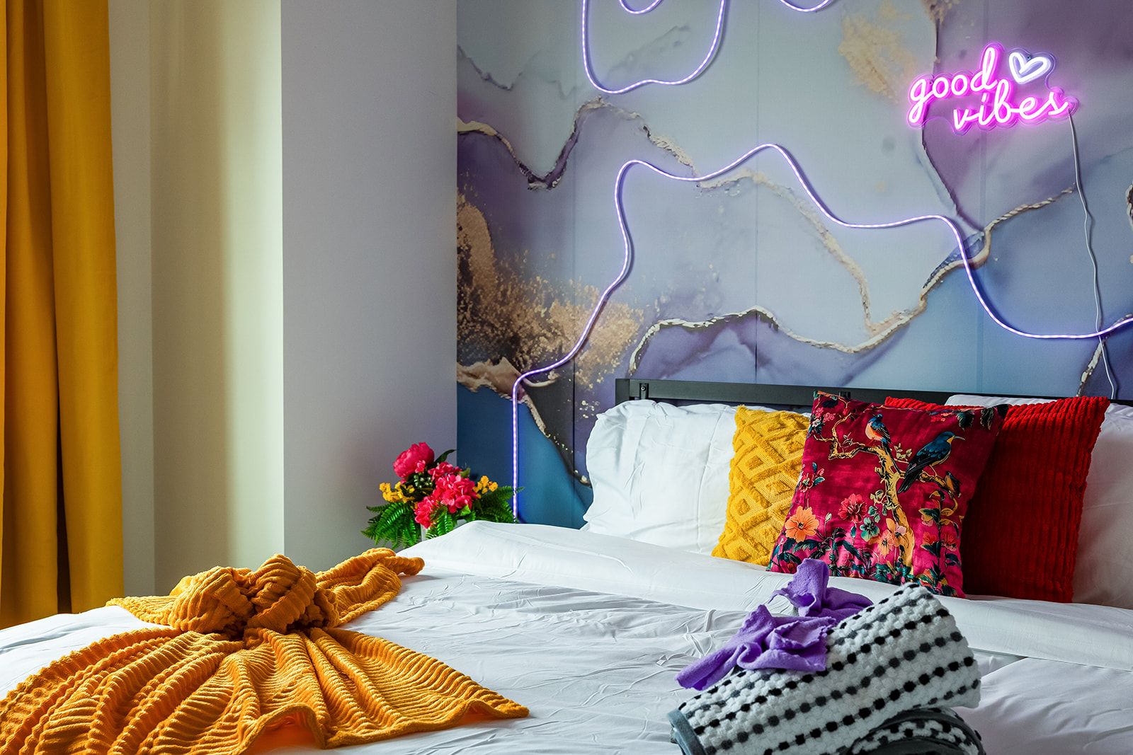 Une chambre d’hôtel avec un lit, un panneau lumineux au néon et un mur orné d’un motif imitant le marbre.