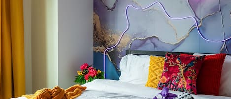 Une chambre d’hôtel avec un lit, un panneau lumineux au néon et un mur orné d’un motif imitant le marbre.