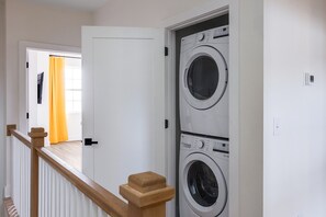 Una sala de bugaderia amb dues rentadores frontals apilades i una escala de fusta que condueix a una sala adjacenta.