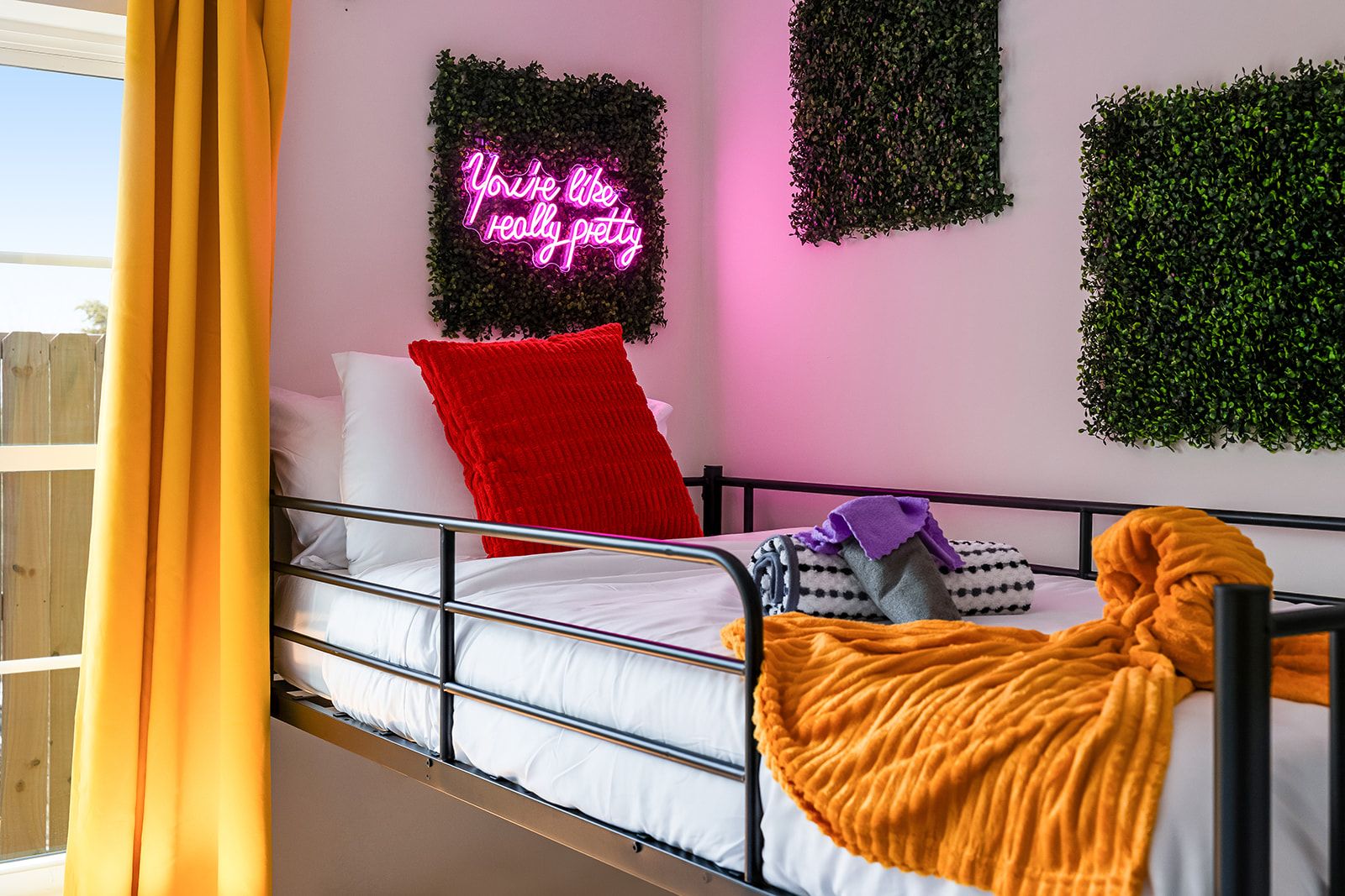 A bunk bed with a neon sign, a red pillow, and a yellow curtain.