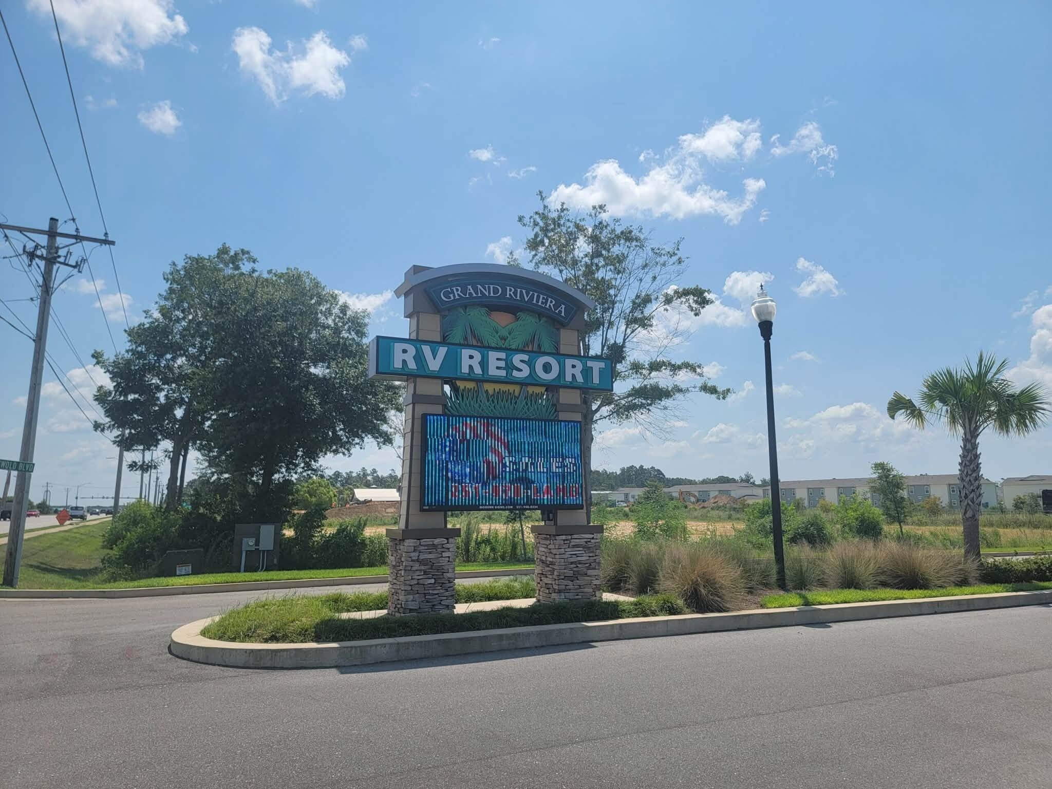 A sign for Grand Riviera RV Resort with a clear sky and palm trees in the background.