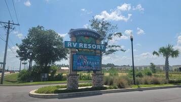 A sign for Grand Riviera RV Resort with a clear sky and palm trees in the background.