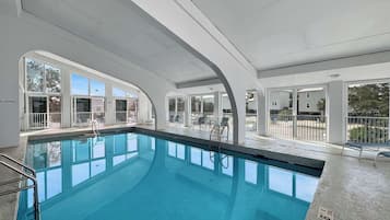 An indoor swimming pool with clear glass walls, a tiled floor, and a metal ladder.