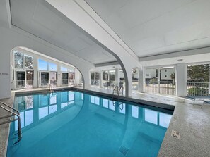 Une piscine intérieure avec des parois en verre transparent, un sol carrelé et un escalier en métal.