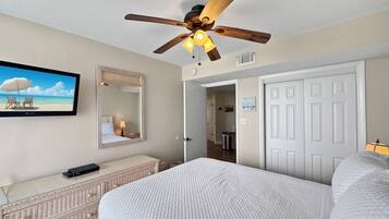 A bedroom with a bed, a ceiling fan, a television, a mirror, and a door leading to a bathroom.